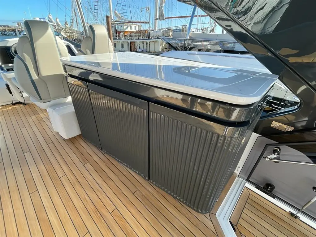 Luxury yacht interior featuring two grey captain seats, a polished table, and sleek cabinetry on a teak deck.